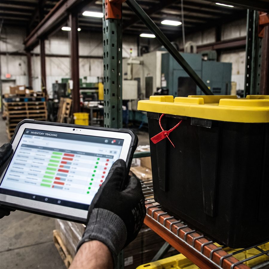A hand holding a tablet showing an inventory tracking dashboard next to a tamper-sealed tote