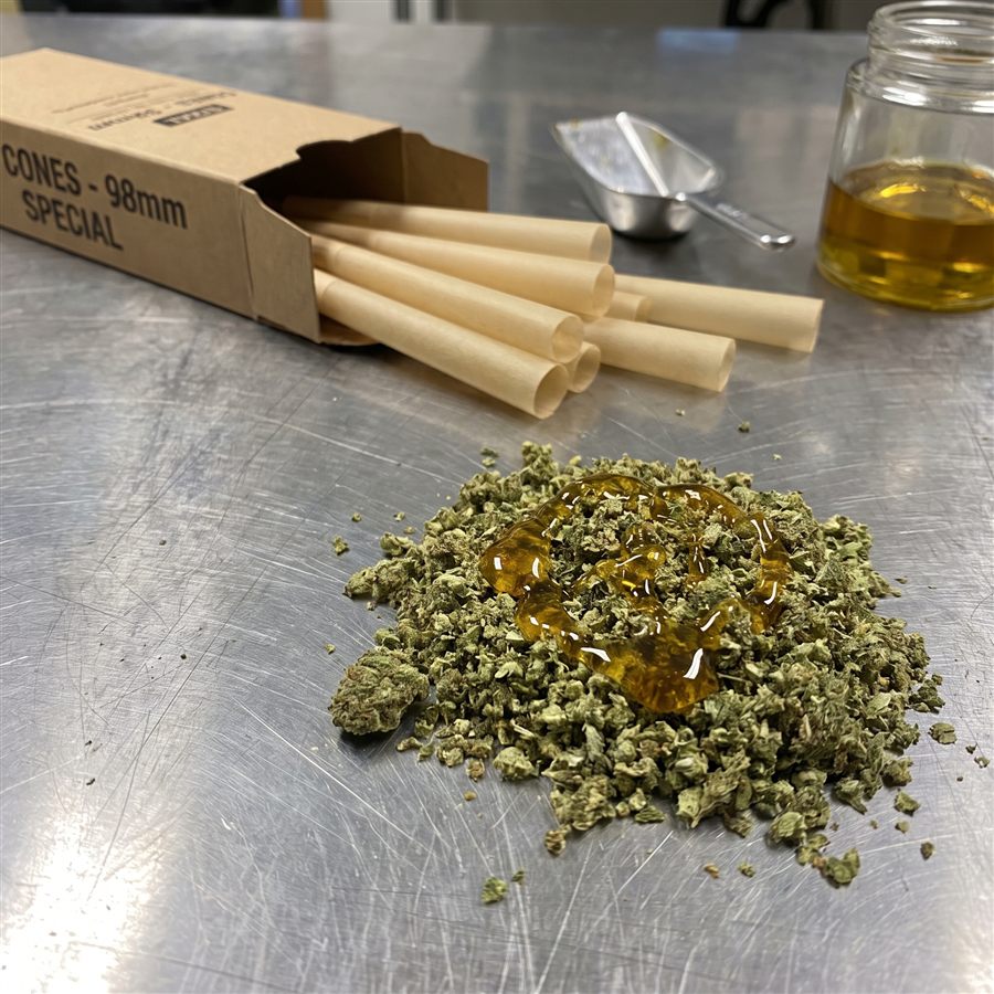 Ground cannabis flower with concentrate worked into it, next to empty pre-roll cones