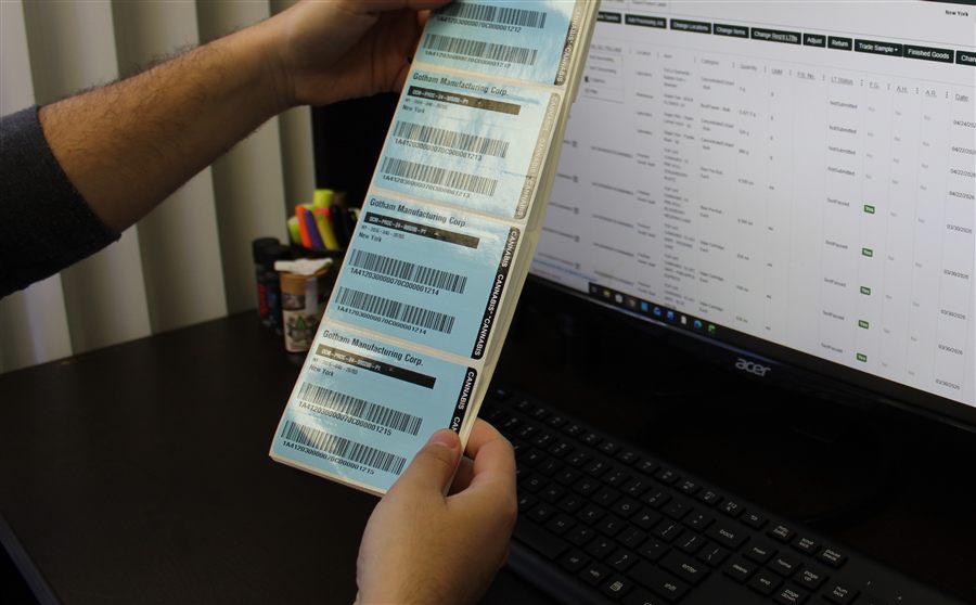 A hand holding real Gotham Manufacturing Corp. regulatory labels in front of the compliance tracking system