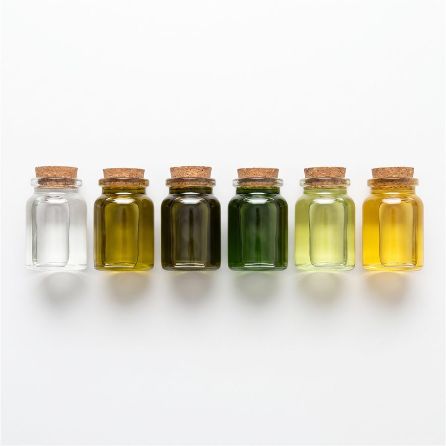 Six small jars of carrier oils side by side, from clear MCT oil to deep green hemp seed oil